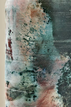 Close-up of a cylindrical vessel with a marbled, textured finish in teal, gray, blush pink, and black, showing horizontal etched or scratched lines across the surface.