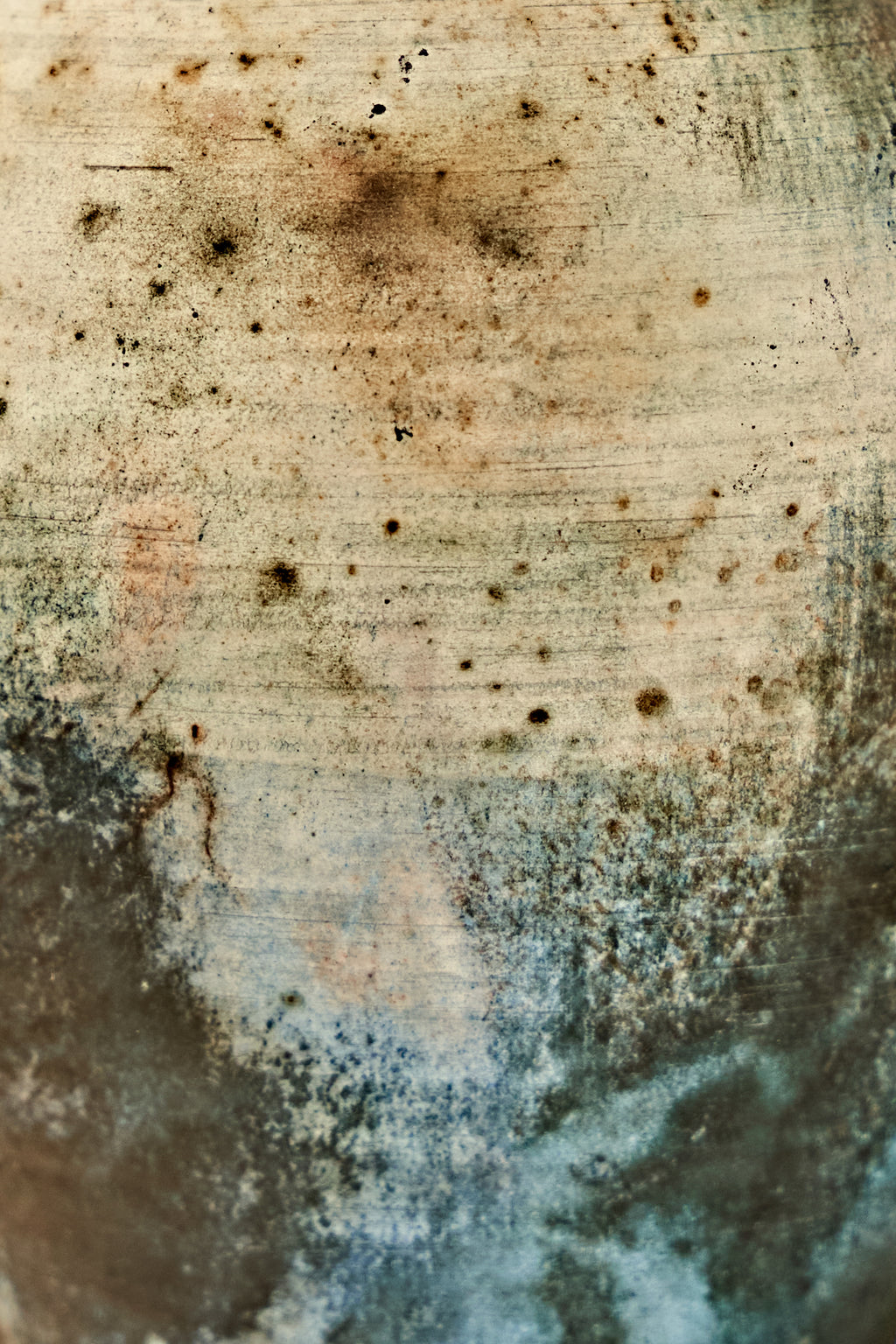 A close-up of a distressed ceramic stone-like surface with a mottled pattern of beige, brown, gray, and blue tones, featuring speckles, stains, and textured brush-like striations.