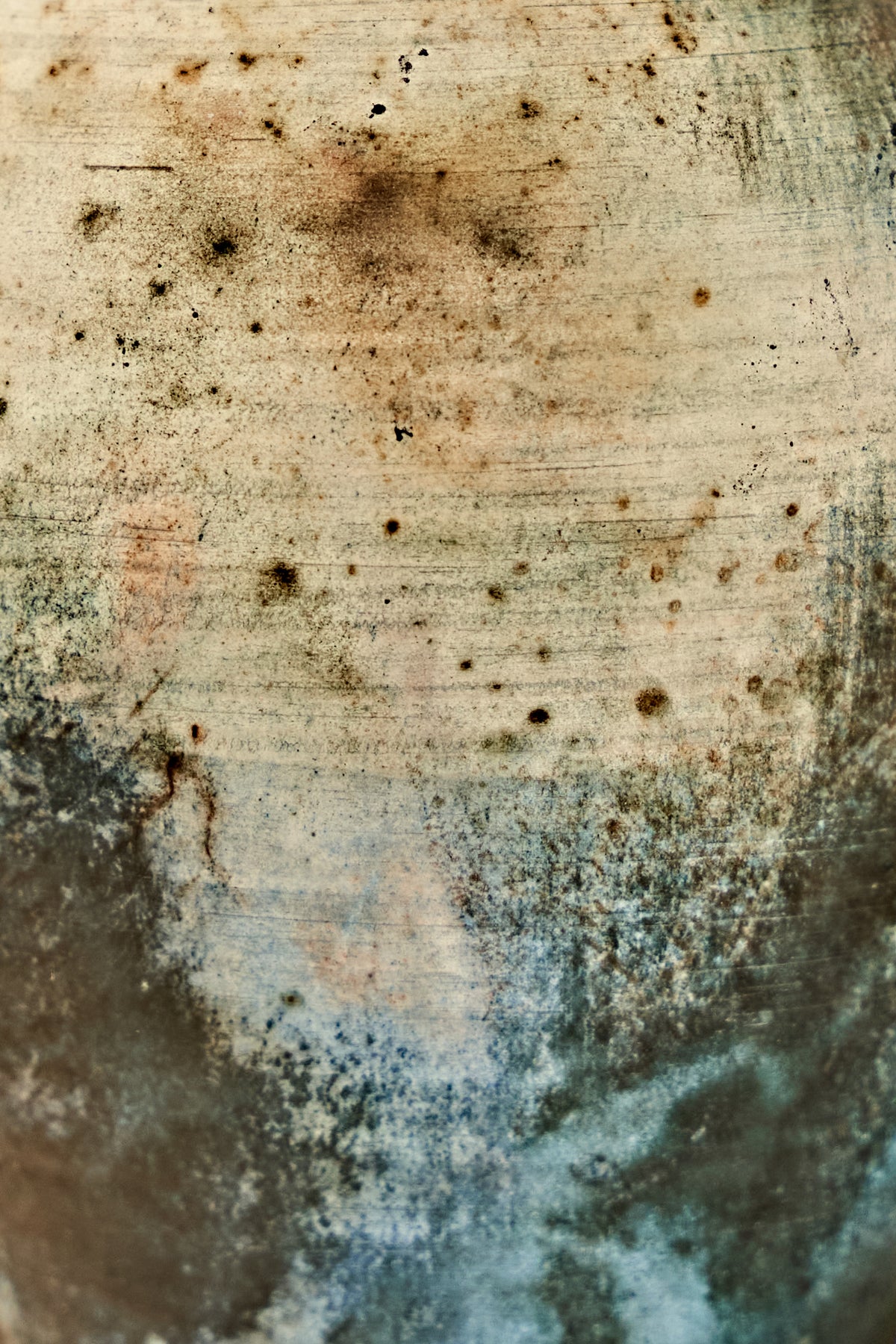 A close-up of a distressed ceramic stone-like surface with a mottled pattern of beige, brown, gray, and blue tones, featuring speckles, stains, and textured brush-like striations.