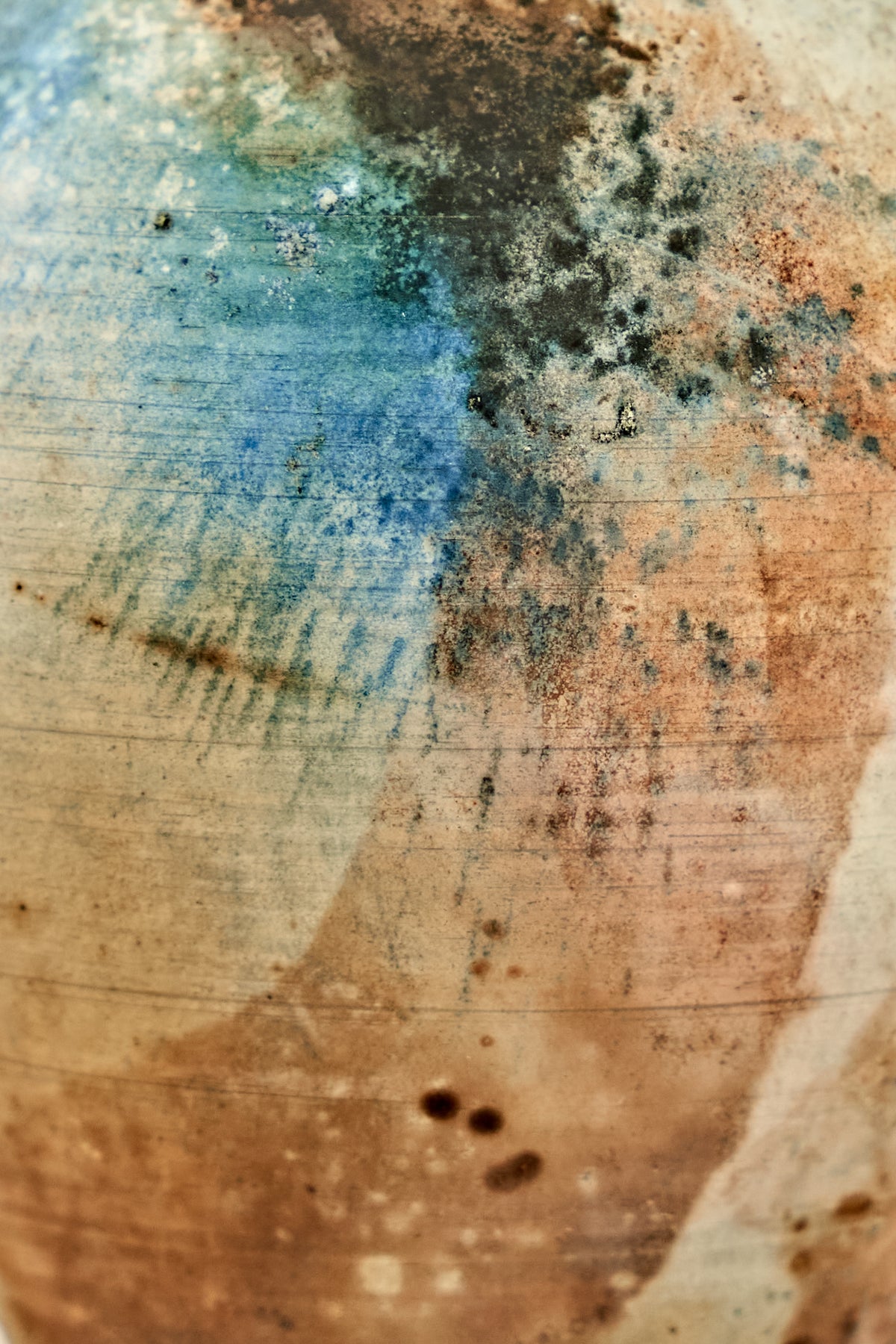 Abstract textured surface with mottled blue, brown, black, and beige tones, resembling a distressed painted or mineral-like pattern.