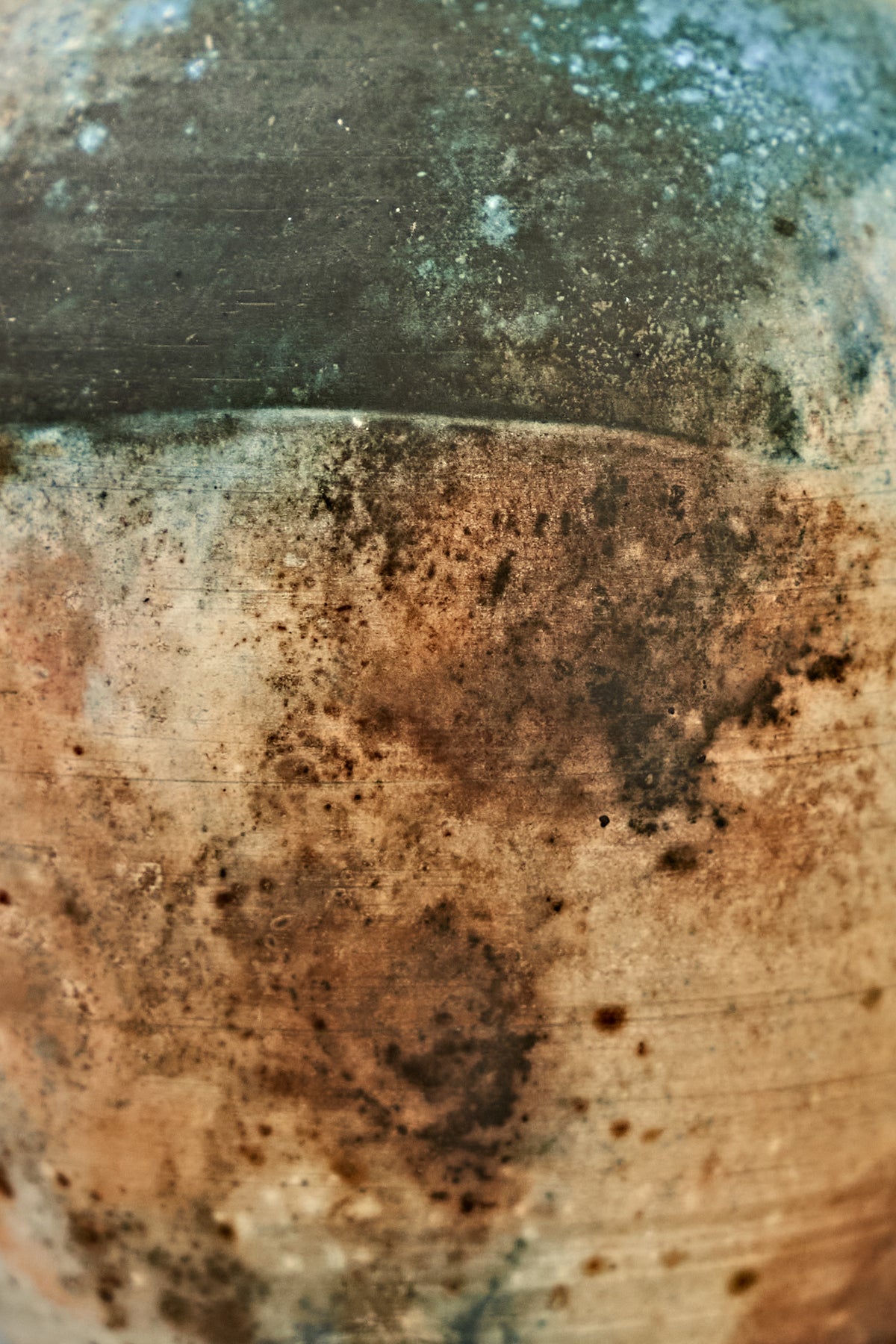 Close-up of a rustic ceramic surface with mottled earthy tones, showing a transition from dark charcoal-gray at the top to warm tan, brown, and black speckling below.